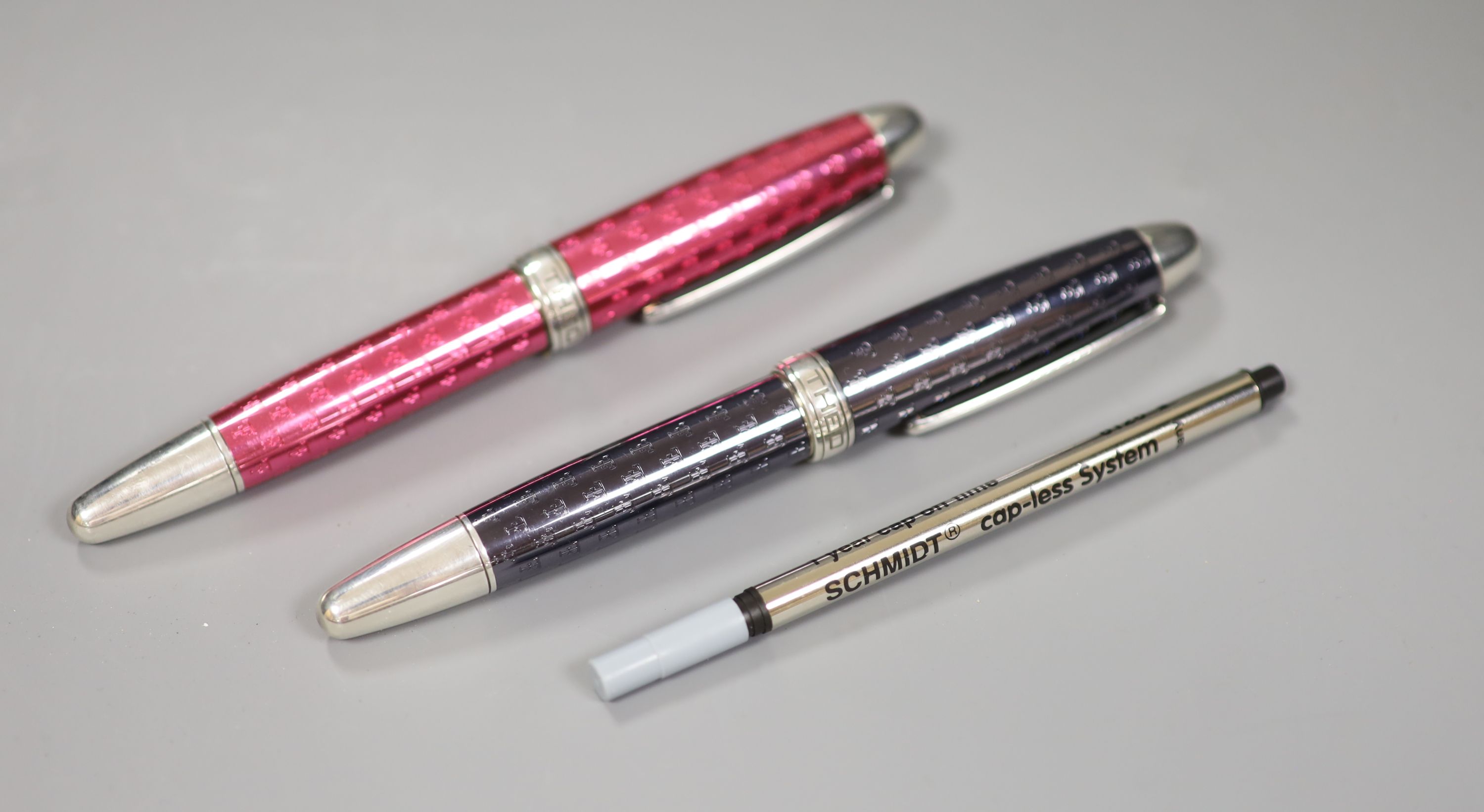Two white metal and enamel roller ball Theo Fennell logo pens, one black and one pink, 14.4 x 10.4cm diameter, both include new black i